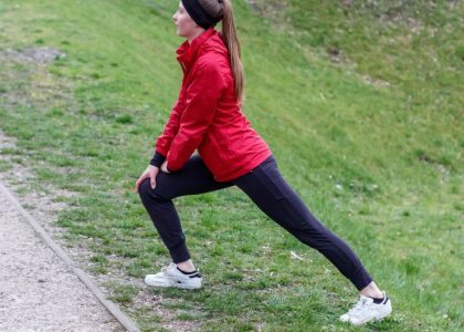 Woman in red jacket stretching in a park, illustrating outdoor fitness and healthy lifestyle.